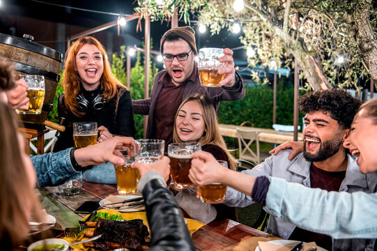 Happy smiling friends having fun drinking out at beer garden -  Young people eating bbq at bar restaurant garden - Life style concept on young people enjoying weekend hangout time together at night .