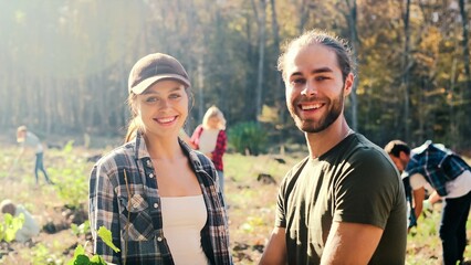 Portrait of young Caucasian joyful happy couple of environmental volunteers talking and smiling to camera in park on sunny day. Planting seedlings of trees concept. Outside. Environmental.