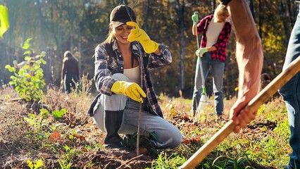 Young happy Caucasian woman bringing seedling of tree and man digging hole in ground to plant it....