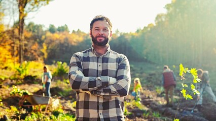 Portrait shot of handsome Caucasian man standing at forest field and looking to camera. Outdoors. Good-looking male, eco volunteer at planting trees day. Gardening and environmental concept.