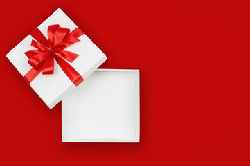 Open white gift box with red ribbon on red background, copy space