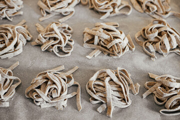 Homemade pasta. Dry fettuccine noodles in nests on baking tray close up. Making whole-grain pasta