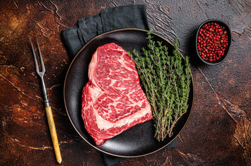 Black Angus Rib Eye steak, raw marbled beef meat with herbs. Dark background. Top view