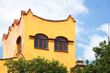 Mexico City, Mexico - The facade of a bright yellow building with red trim, built in a traditional Mexican colonial style.  Image has copy space.
