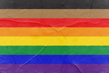 Pride rainbow flag with black and brown stripes painted on cracked textured wall. Outdoor Grunge...