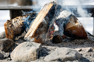 Close up of an outdoor fire pit with burning embers and smoke during winter