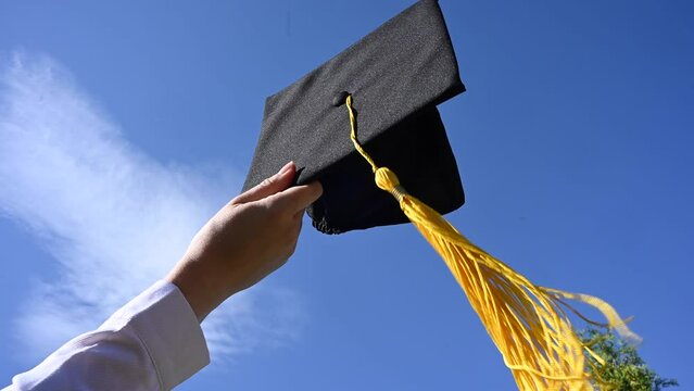 Close-up of a woman's hand with a graduation cap against the blue sky. 