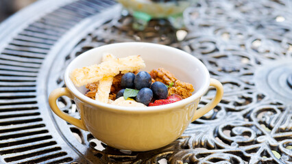 Little dessert bowl with greek yogurt and fruits on an ornamented iron table. Cup of meal on a table.
