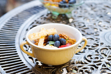 Little dessert bowl with greek yogurt and fruits on an ornamented iron table. Cup of meal on a table.