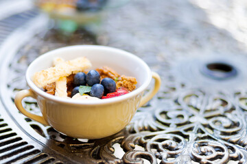Little dessert bowl with greek yogurt and fruits on an ornamented iron table. Cup of meal on a table.