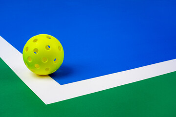 Indoor Pickleball on the court line.  Yellow Pickleball with Blue interior, white line and green exterior..