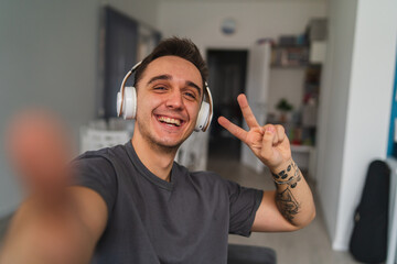 A young guy is taking a selfie or talking on a video call while using his phone on a couch in his house during the day