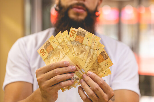 Um homem segurando notas do Real Brasileiro. Notas de 50 Reais. Leque de dinheiro. Economia brasileira e neg&oacute;cios.