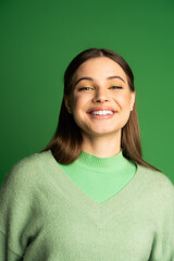 Fototapeta premium Portrait of happy teen girl in jumper smiling at camera isolated on green.
