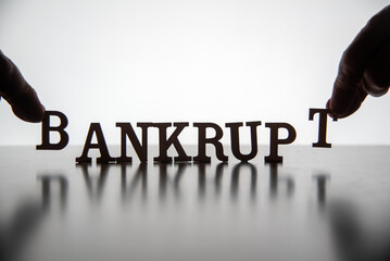 Hands placing the letters for the word BANKRUPT in silhouette backlit on reflective surface. 