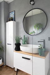 Modern interior of bathroom with white furniture and cabinet, round mirror on the grey wall, ceramic washbasin with faucet. Scandinavian design and minimalism. Vertical.