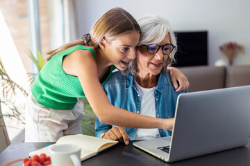 Happy granmother using laptop with her granddaughter at home.