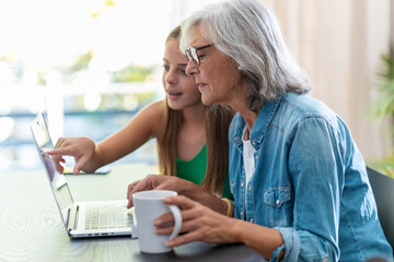 Shot of happy granmother shopping online with credit card using laptop with her granddaughter at home.