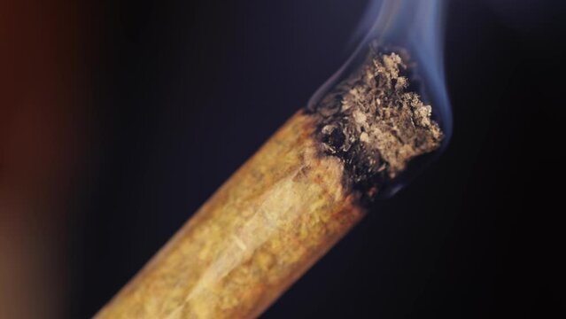 Woman lights a big CBD weed Joint conical cigarette or a drug joint with a lighter macro close up, Medical Marijuana smoking
