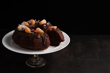 On a black background with a place for writing text on a stand, a chocolate cake is decorated with fruits.