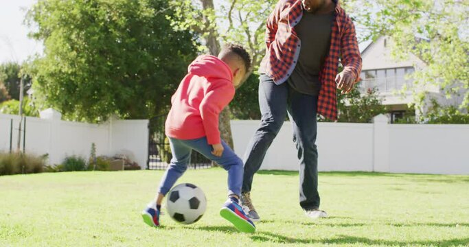 Happy african american father and his son playing football in garden