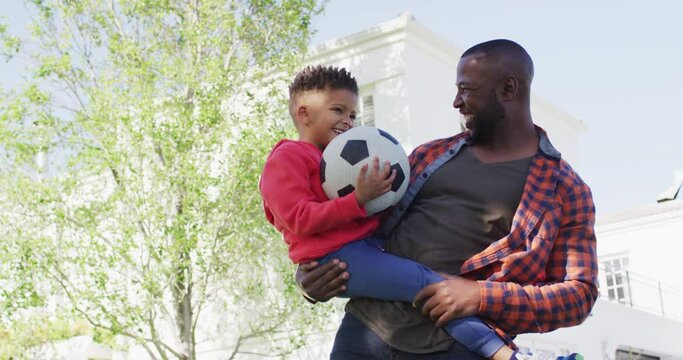 Portrait of happy african american father and his son holding football and embracing in garden