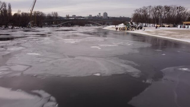 the drone flies over the hole in the winter river, the river is covered with ice, people enter the cold water, cross themselves and plunge headlong into the ice water three times
