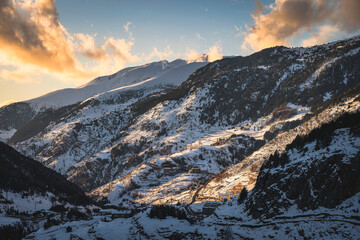 El Tarter village in a valley between mountains. Sunset light illuminating side of a mountain and clouds. Ski winter holidays, Andorra, Pyrenees - obrazy, fototapety, plakaty