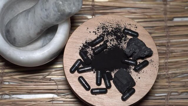 Natural active charcoal from capsules displayed on wooden stand with mortar in the background.