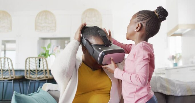 Happy african american granddaughter putting vr headset on grandmother at home, copy space