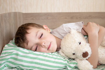adorable boy sleeping in bed with bear toy. six year old baby sleeping at home