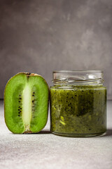 Homemade kiwi jam in a jar and kiwi slyces on concrete background with copy space