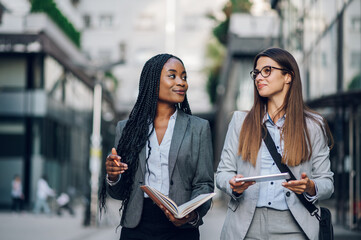 Two multiracial business woman meeting outside and using a tablet