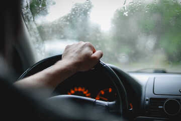 Young caucasian guy keeps his hand on the steering wheel while driving a car on a rainy day