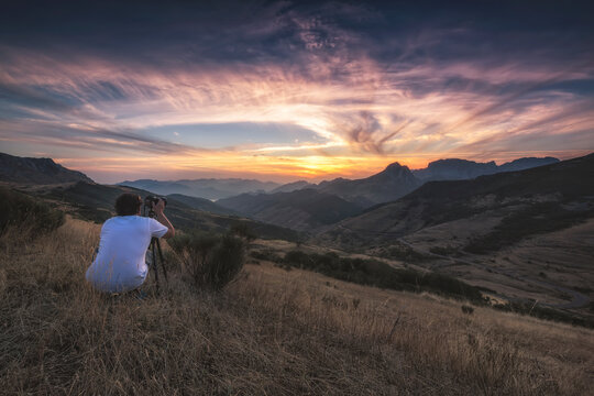 Young man photographing the sunset on top of a mountain.