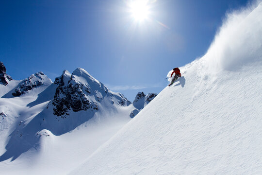 Skier making a turn with mountain and sun backdrop.