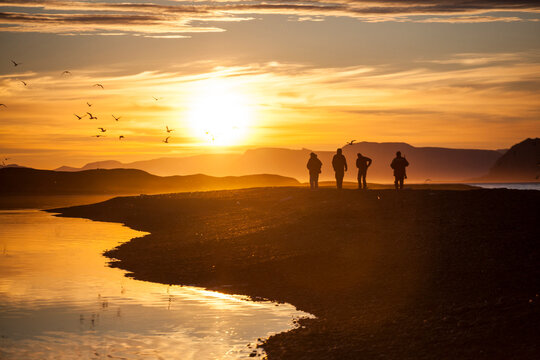 Men hike the beach at sunset to visit a research outpost in Calypsobyen, Svalbard.