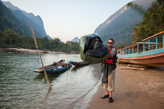 Man deflating inflatable boat on Nam Ou river shore, Muang Ngoi, Phongsaly, Laos