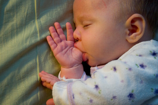 A two month old baby sucking her thumb.
