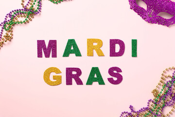 Mardi Gras background. Mardi gras lettering with carnival mask and beads on pink background.