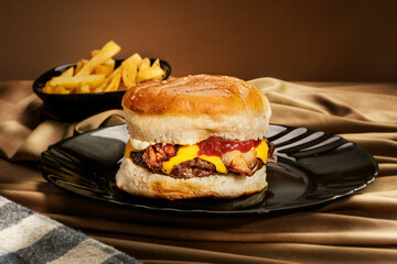 Una hamburguesa de bacón con queso cheddar sobre un plato negro y papas fritas 