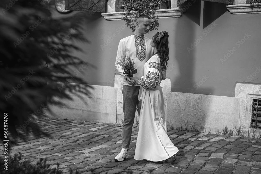 Canvas Prints black and white photo, Emotional portrait of happy young couple in love, family hugging, holding hands, running in Lviv city in traditional Ukrainian shirts. Young people hug in the old town of Lviv