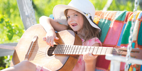 Little girl musician playing guitar. Happy cute teen girl swinging and having fun healthy summer vacation activity. Spring and kid. Banner for website header. Kids music and songs.