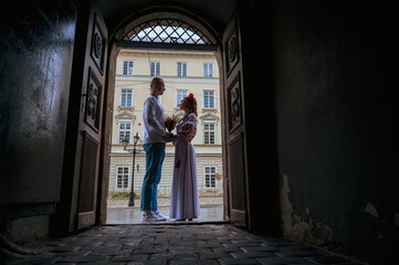 Fototapeta na wymiar Emotional portrait of a happy young couple in love, a family hugging, holding hands in the city of Lviv in traditional Ukrainian shirts, holding hands. Young people hug in the old town of Lviv