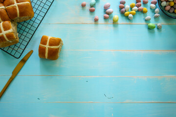 Hot cross buns cooling on a wire rack with speckled easter eggs on a blue painted timber wooden...