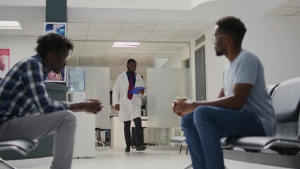 Medical staff doing examinations with african american people, patients with illness waiting in hospital lobby. Group of men sitting in waiting area before attending appointment. Tripod shot.