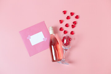 Envelope, bottle of wine and glass with glass hearts on pink.