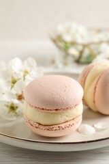 Delicious pink macarons and flowers on white wooden table, closeup