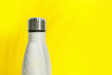 Stylish white thermo bottle with water drops on yellow background, closeup. Space for text