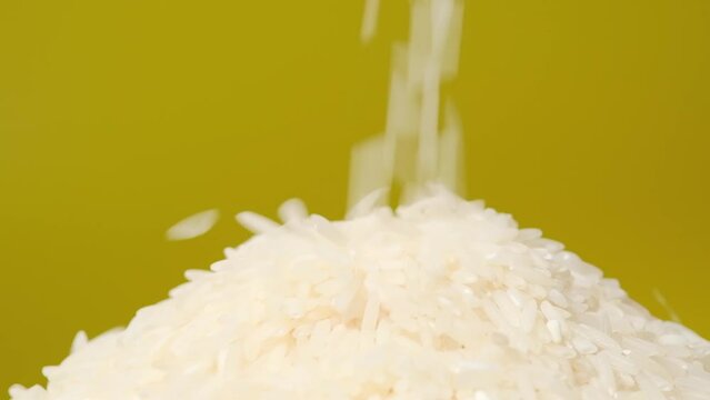 Closeup macro video rice grains falling down on white round uncooked rice rotating on yellow background. 